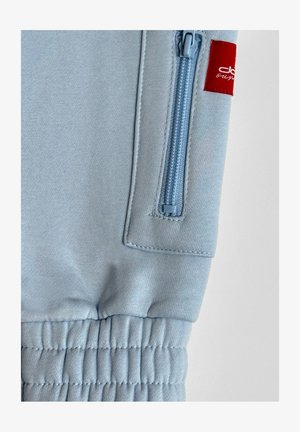 Hellblaue Jogginghose mit einem gerippten Bund, ausgestattet mit einer Reißverschlusstasche in einer passenden Farbe und einem kleinen roten Logotag.