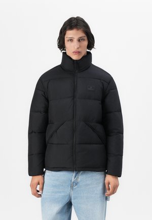 Black padded jacket with a high collar, zip closure, and two front pockets. Made of a smooth fabric, featuring a logo patch on the chest.