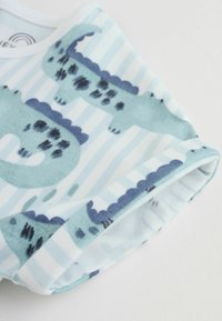 Pamučne kratke hlače sa svijetlom plavom i bijelom prugastom uzorkom. Sadrže stilizirane krokodilske motive u tamnijoj plavoj boji s crnim naglascima.