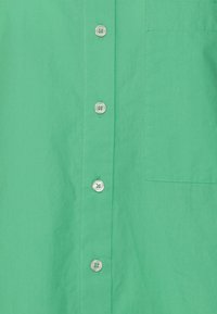 Green button-up shirt with a smooth texture, featuring six round buttons and a chest pocket. Simple, clean style with a solid color.