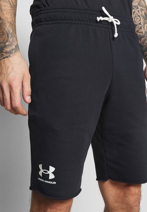 Mężczyzna noszący czarne szorty Under Armour z białym logo, ściągaczem w pasie i tatuażami na ramionach widocznymi od połowy uda do talii.
