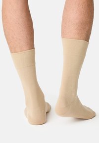 Beige sokker lavet af blødt, strækbart materiale. De har en ribbet top og en glat struktur, der sidder tæt om anklen og foden.