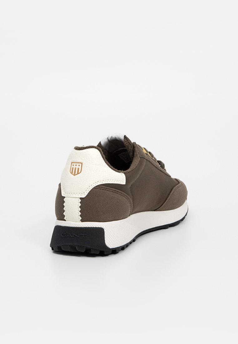 Brązowe trampki z gładkim materiałem wierzchowym, białymi akcentami na pięcie, czarną podeszwą oraz teksturowanym wykończeniem. Logo z tyłu.