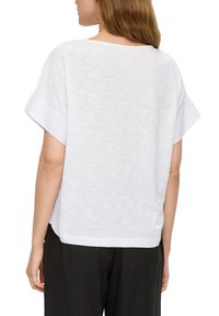 Haut blanc à manches courtes avec une coupe décontractée et une texture légère. Doté d'un large col et d'une finition lisse en bas.