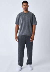 Camiseta gris de gran tamaño con cuello redondo, que presenta un logotipo sutil en el pecho; combinada con pantalones sueltos gris a juego y zapatillas blancas.