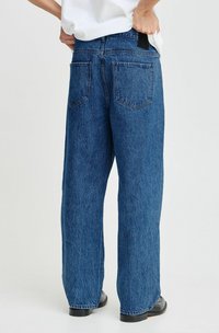 Jeans de denim azul de pierna ancha con un acabado texturizado, que cuentan con dos bolsillos traseros y una etiqueta negra en la cintura.