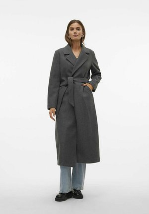 Manteau en laine grise avec ceinture, revers crantés et poches latérales. Porté sur un jean large bleu et des chaussures noires. Texture lisse.