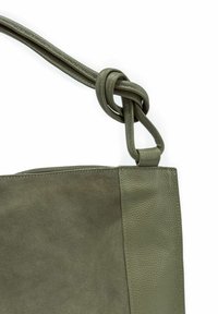 Sac fourre-tout en cuir vert olive avec une finition en daim texturé et des accents lisses. Doté d'une bandoulière nouée et d'un design minimaliste.