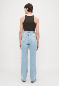 Brun ärmlös topp som matchas med ljusblå högmidjade jeans. Jeansen har en svag flare och bakfickor. Minimalistisk design, inga mönster.