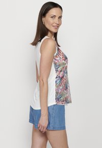 Witte mouwloze top met een kleurrijke, geprinte stof aan de voorkant en zijkanten. Gecombineerd met denim short.