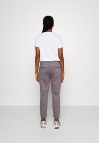 Grå skräddarsydda byxor med en slät textur, med bakfickor, kombinerade med en enkel vit t-shirt, sett bakifrån.