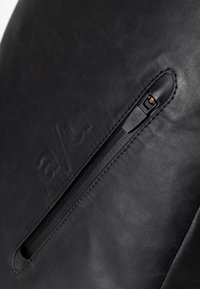 Borsa nera in pelle con chiusura a zip, dettaglio del logo impresso e superficie liscia. Design minimalista con linee eleganti e accenti sottili.