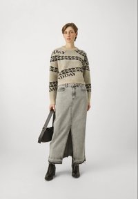 Κοντομάνικος μπλε ζακέτα με μαύρο κείμενο και σχέδιο αλυσίδας, συνδυασμένη με μακριά φούστα από γκρι τζιν με μπροστινό άνοιγμα και φθαρμένο τελείωμα. Μαύρες μπότες έως τον αστράγαλο και τσάντα.