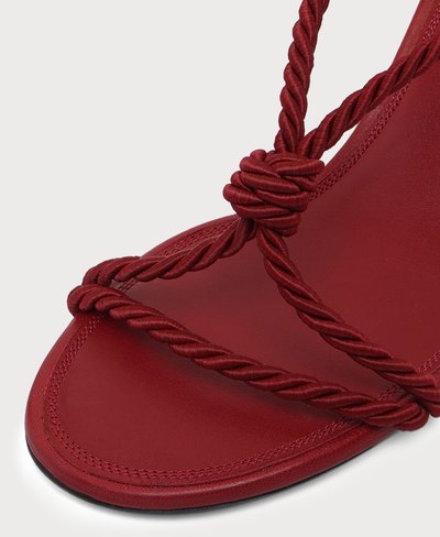 Gros plan d'une sandale rouge avec des lanières en corde torsadée et un détail de nœud sur une semelle intérieure en cuir lisse.