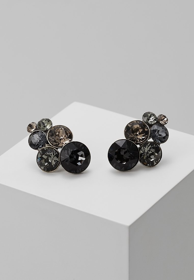 Boucles d'oreilles rondes présentant un cluster de cristaux étincelants dans des nuances de noir, gris et taupe, montés sur une base métallique argentée.