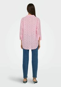 Camicia rosa chiaro con dettagli in pizzo, maniche 3/4 e colletto. Abbinata a jeans in denim blu e sandali neri con tacco.