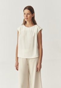 Blusa blanca de mangas cortas hecha de un tejido ligero, con un escote redondo y un corte holgado, combinada con pantalones de pierna ancha en color beige.
