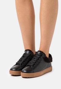 Svarta lädersneakers med en texturerad brun gummisula och fuzzy svart kant runt vristen. Har snörning och präglad logotyp.