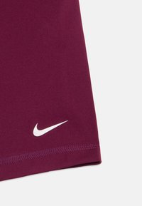 Burgunderfarget stoff med hvit Nike swoosh-logo nær den sydd kanten, sannsynligvis en del av ermet på et plagg eller buksebein mot en hvit bakgrunn.