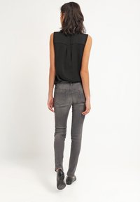 Top negro sin mangas con detalles de plisado en la parte posterior, combinado con jeans ajustados grises y zapatos negros de slip-on, visto desde la vista trasera.