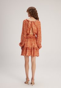 Orangenes, gemustertes Kleid mit langen Ärmeln, gerafften Kanten und einem Rückenausschnitt. Kurzer, schwingender Rock mit gerafftem Taillendetail.