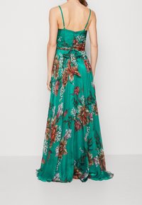 Long, sleeveless dress made of smooth teal fabric featuring a floral pattern in orange, pink, and white. Ties at the waist enhance the silhouette.