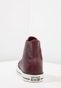 Baskets montantes en cuir bordeaux avec surface texturée, semelle en caoutchouc blanche, accents rayés noir et blanc, et patch logo Converse All Star.