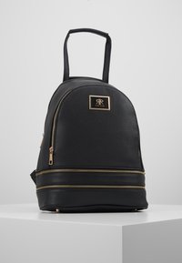 Czarny plecak z fakturowanej ekoskóry o zaokrąglonym kształcie, z złotymi suwakami i metalową blaszką z logo z przodu.