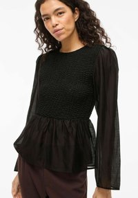 Top nero con peplum caratterizzato da un bustino in maglia testurizzata e maniche lunghe semi-trasparenti, con vita arricciata e orlo liscio.
