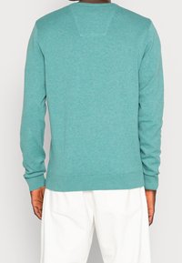 Turkusowy sweter z długimi rękawami i okrągłym dekoltem. Ma prążkowane mankiety i dół, wykonany z miękkiej, teksturowanej dzianiny.