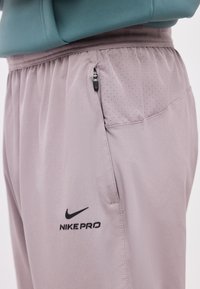 Κοντινή λήψη από αθλητικό σορτς Nike Pro ανοιχτόμωβ με φερμουάρ σε πλαϊνή τσέπη και λεπτομέρεια με διάτρητο δίχτυ κοντά στη μέση.