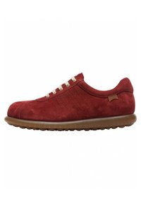Sneaker rossa in suede con punta arrotondata, lacci beige chiaro e superficie texture. Caratterizzata da una suola in gomma marrone flessibile e strisce laterali sottili.