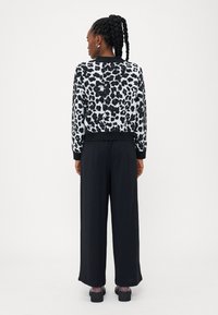 Sweter w cętki jawy w odcieniach czerni i bieli z prążkowanymi mankietami, zestawiony z czarnymi spodniami typu wide-leg i masywnymi czarnymi butami. Czysty, minimalistyczny design.