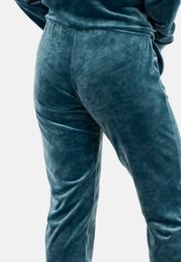 Gros plan sur une personne portant un pantalon en velours bleu au toucher doux, mettant en valeur la brillance et les plis du tissu.
