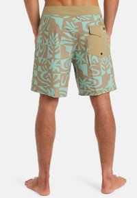 Bañador beige con patrones de hojas en teal, cinturilla elástica y un bolsillo trasero con tapa. Fabricado con tela de secado rápido.