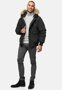 Sort pufferjakke med faux fur hætte, to forlommer og lynlåsdetaljer, parret med en grå rullekrave og mørkegrå slim-fit bukser.