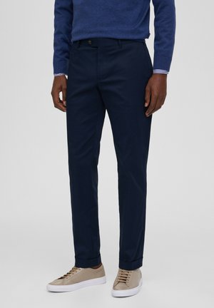Pantaloni navy con vestibilità dritta, realizzati in tessuto liscio. Presentano una chiusura con bottone, tasche frontali e polsini alla caviglia, abbinati a sneakers beige.