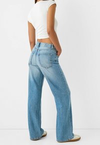 Ljusblå vida jeans med hög midja, två bakfickor och förvissad textur. Matchas med en figurnära vit t-shirt med kort ärm.