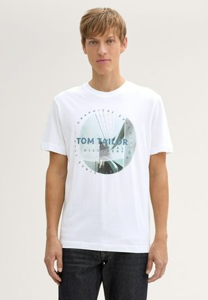 Hvid bomulds t-shirt med en cirkulær grafik i blå med teksten "TOM TAILOR" og abstrakte designelementer. Korte ærmer og rund hals.