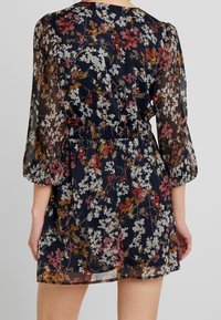 Blommig klänning med puffiga, veckade ärmar. Mörk marin bakgrund med färgglada blommor i rött, gult och vitt. Elastisk midja.