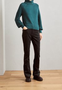 Teal knitted sweater with textured sleeves, paired with black corduroy pants and chunky black platform boots. Wood flooring background.