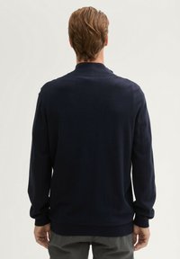 Granatowy sweter wykonany z miękkiego materiału, z klasycznym kołnierzykiem i długimi rękawami. Żebrowania przy mankietach i u dołu zapewniają dopasowane wykończenie.