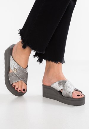 Sandali wedge in velluto grigio con cinturini incrociati e un bottone decorativo, su una suola piattaformata textured di un grigio scuro.