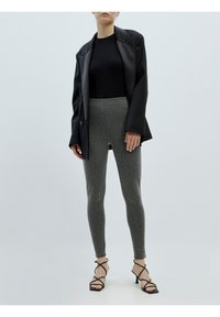 Zwarte blazer over een aansluitende zwarte top, gecombineerd met grijs gestreepte leggings en zwarte sandaaltjes met hoge hakken. Glad textuur overal.