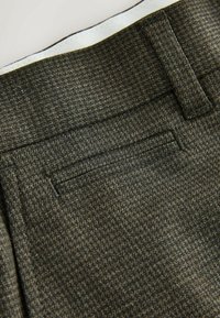 Dark green textured fabric with a houndstooth pattern, featuring a jetted pocket and contrasting white inner waistband.