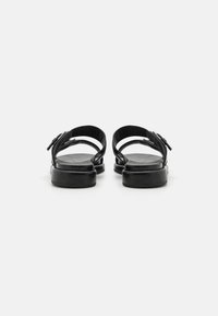 Zwarte leren sandalen met een platte zool, open achterkant en verstelbare bandjes. Gladde textuur met een minimalistisch ontwerp.