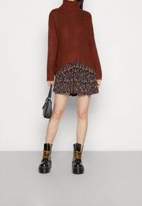 Rust-orange knitted sweater with high collar, layered over a dark floral skirt. Black chunky lace-up ankle boots with yellow laces.