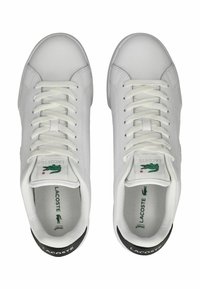 Bílé tenisky s hladkým koženým povrchem, kulatou špičkou, plochými bílými tkaničkami, zeleným logem na jazyku a černými akcenty na patě.