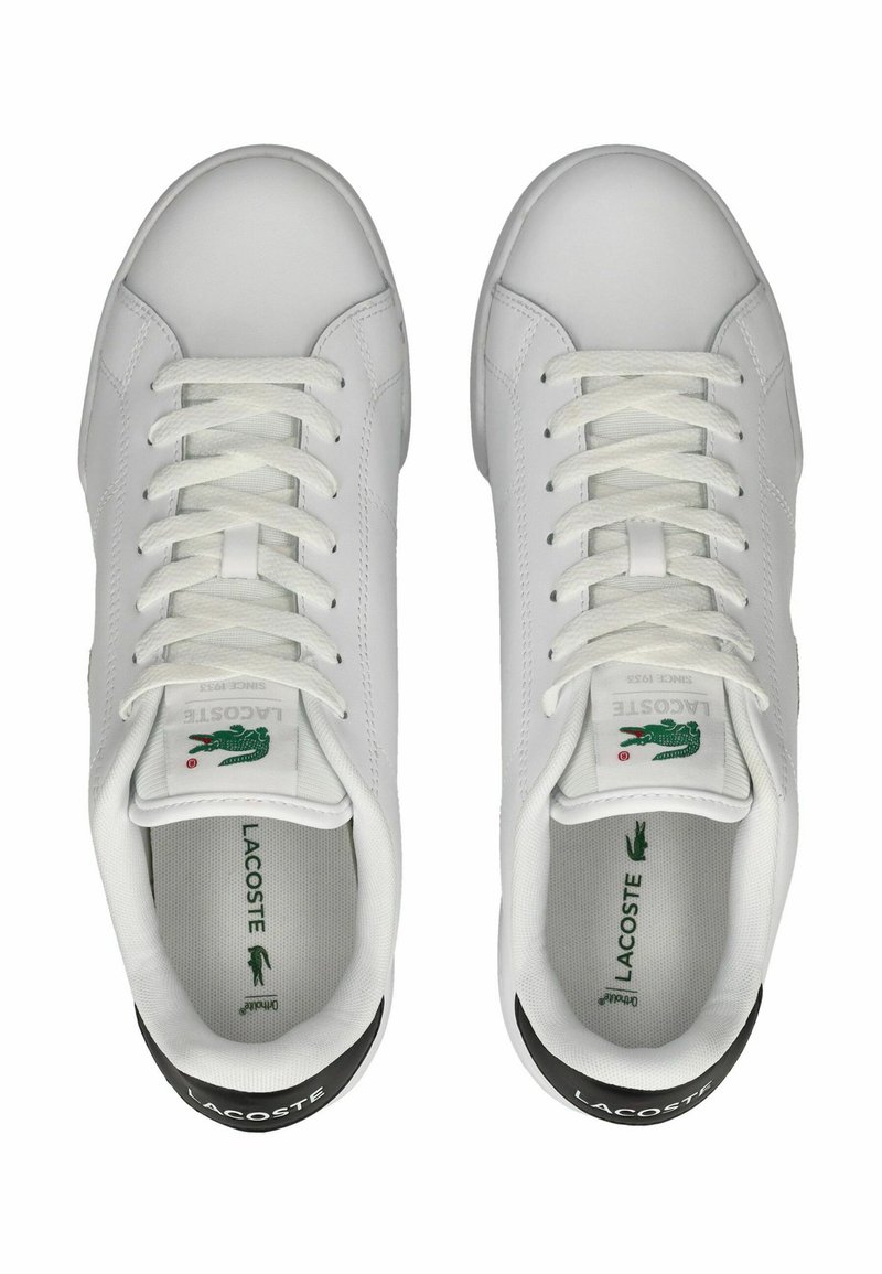 Baskets blanches avec une finition en cuir lisse, bout rond, lacets blancs plats, détail du logo vert sur la languette et accents noirs au niveau du talon.