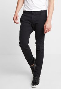 Black slim-fit pants made of denim, featuring a button closure, belt loops, and a smooth texture, paired with black high-top sneakers.